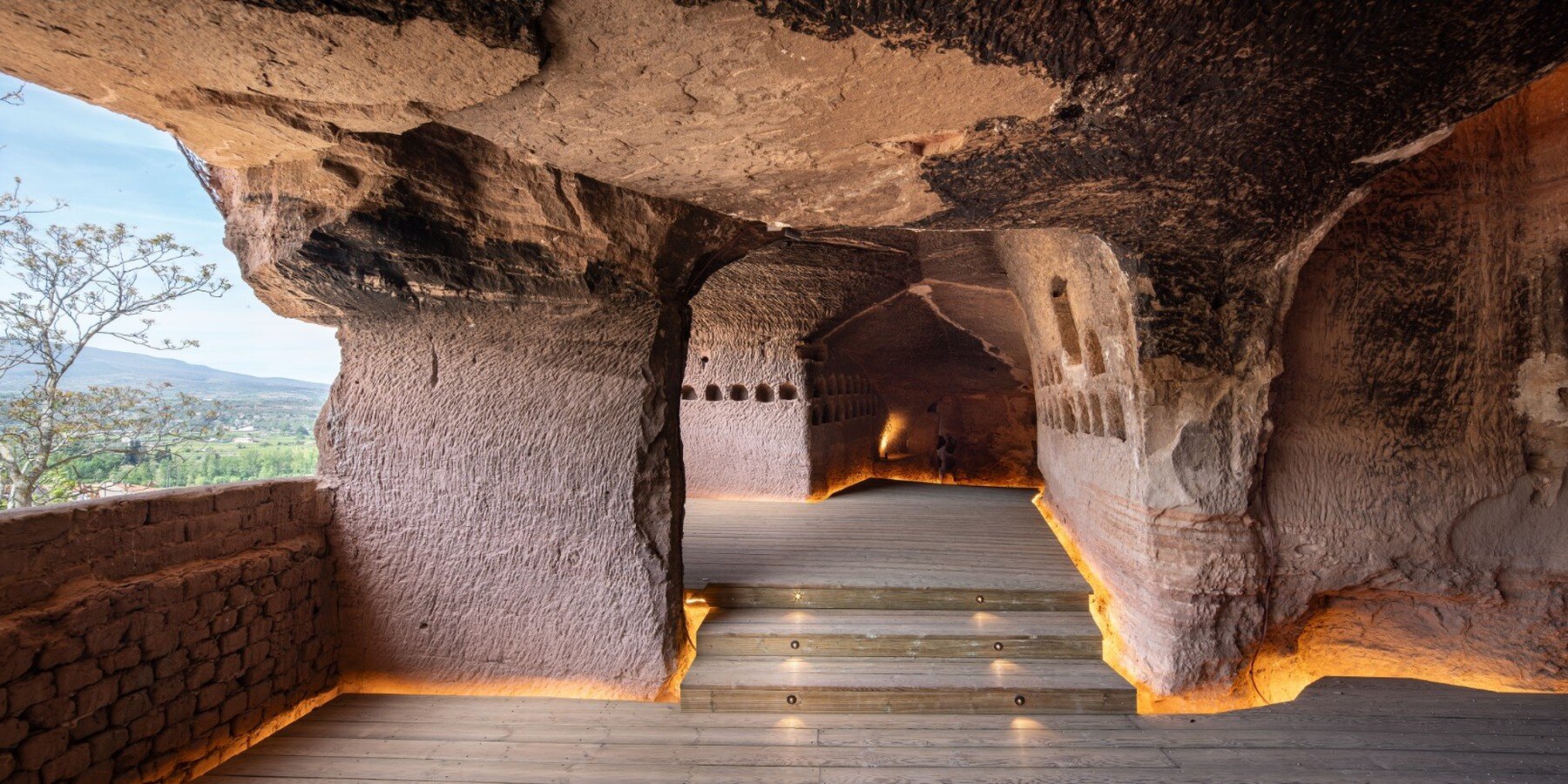 Каменные своды Peña de las Bodegas с деревянными ступенями и подсветкой