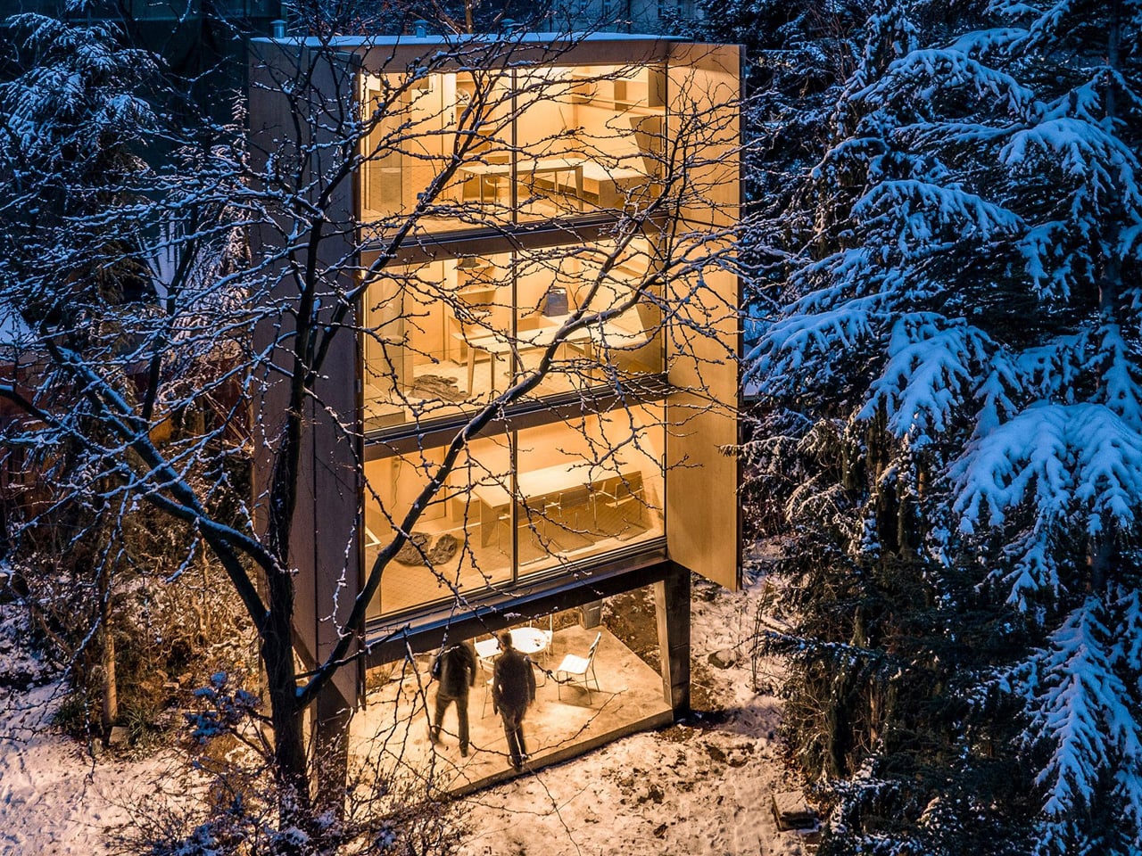 Wardrobe House среди заснеженных деревьев с освещёнными комнатами
